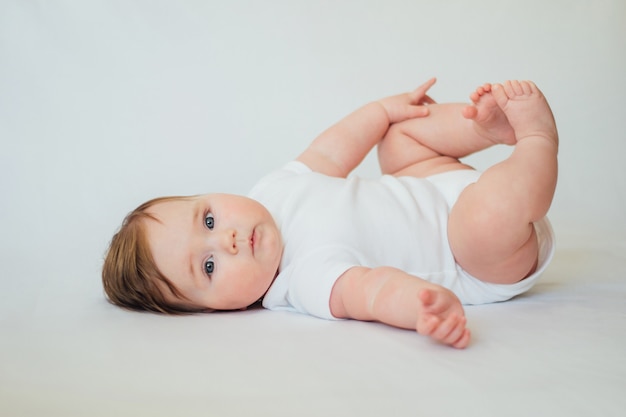 Bébé mignon bébé couché sur le dos sur blanc portant des vêtements blancs.