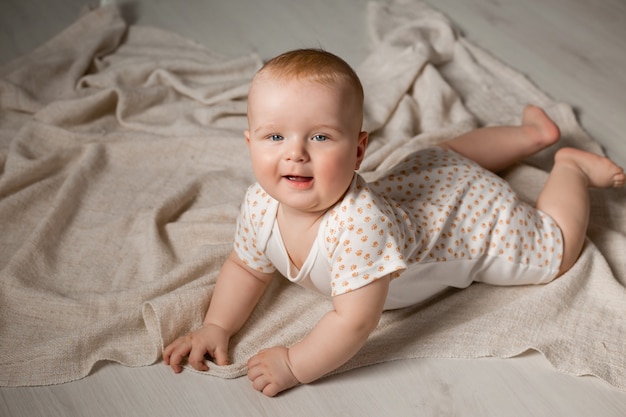 Un bébé mignon dans un body est allongé sur le ventre sur le plancher en bois avec une couverture à la maison