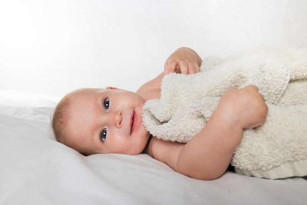 Un bébé mignon d'un demi-an dans une couche et une serviette se trouve sur le dos et regarde joyeusement la caméra