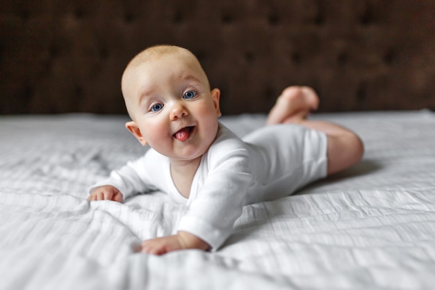 Bébé mignon drôle dans un body léger blanc sur le lit à la maison à la recherche