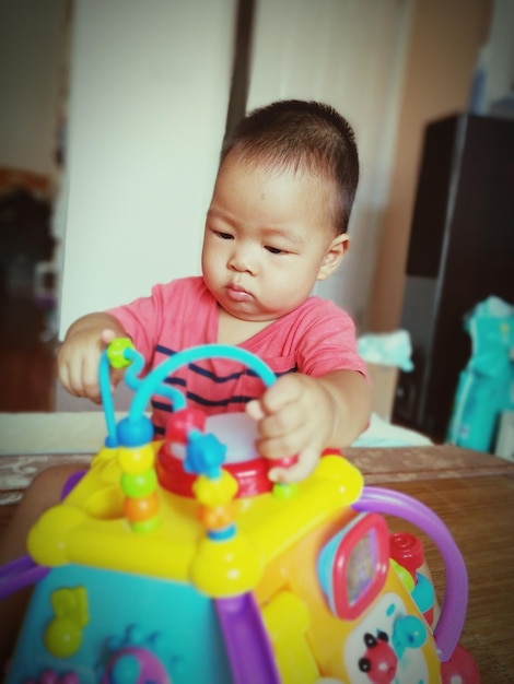 Photo bébé mignon jouant avec des jouets alors qu'il est assis sur la table à la maison