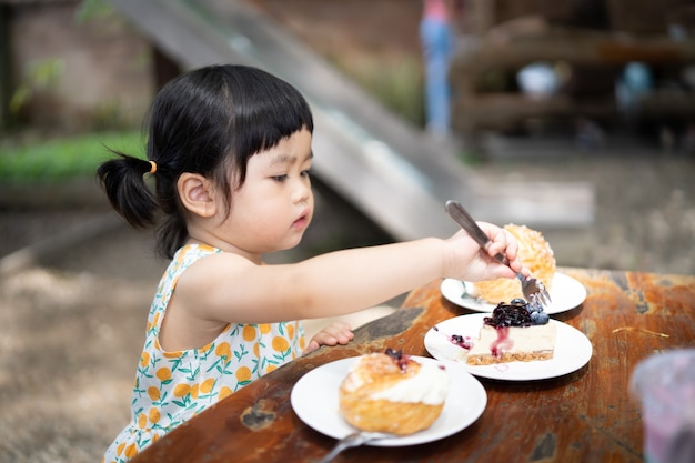 Bébé mignon mangeant le gâteau et s'asseyant sur la table au café