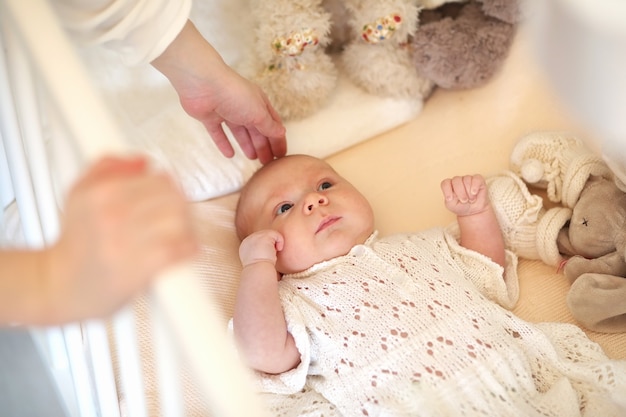 Le bébé mignon nouveau-né se trouve dans le berceau et regarde la mère