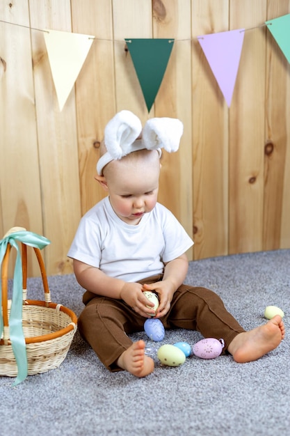 Un bébé mignon avec des oreilles de lapin est assis et joue avec des oeufs de Pâques Pâques