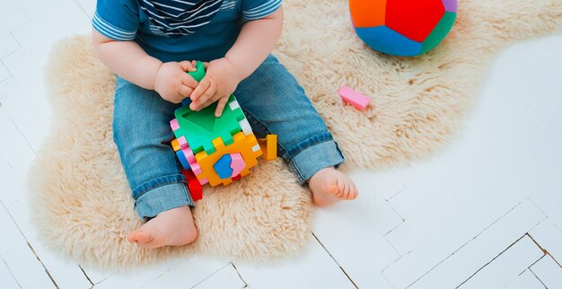 Le bébé mignon s'assied sur le plancher de la maison jouant avec les jouets éducatifs colorés