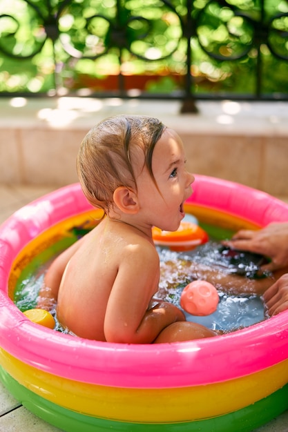 Un bébé mouillé mignon avec la bouche ouverte est assis dans une mini piscine gonflable