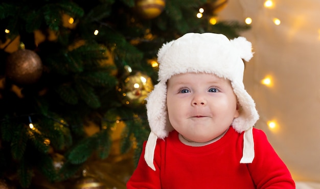 Le bébé de Noël sourit. Une jolie petite fille vêtue d'une robe rouge et d'un chapeau blanc exprime des émotions.