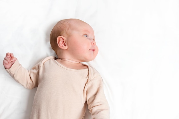 Bébé nouveau-né en body beige regarde de côté allongé sur le lit