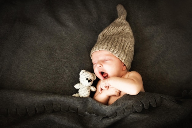 Bébé nouveau-né dormant avec un jouet à côté de l'ours en peluche tricoté et des bâillements.