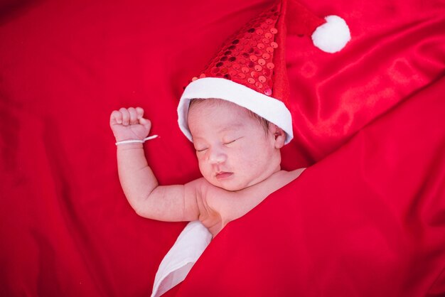 Bébé nouveau-né dormant sur santa het et fond rouge