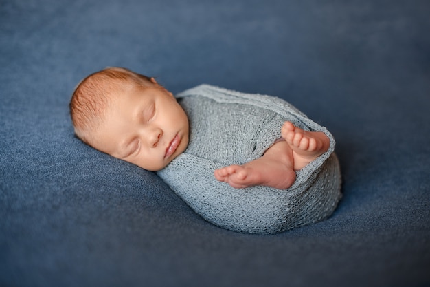 Bébé nouveau-né endormi est enveloppé dans un tissu tricoté gris-bleu