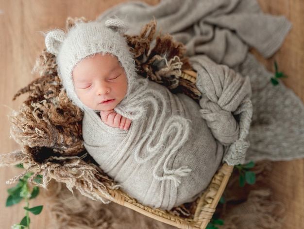 Bébé nouveau-né garçon dormant emmailloté dans une couverture tricotée douce dans un joli panier en osier