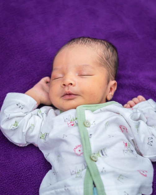 Bébé nouveau-né isolé dormant dans un tissu blanc avec un fond violet d'un angle différent