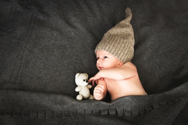 Bébé nouveau-né avec un jouet se trouvant à côté de l'ours en peluche tricoté