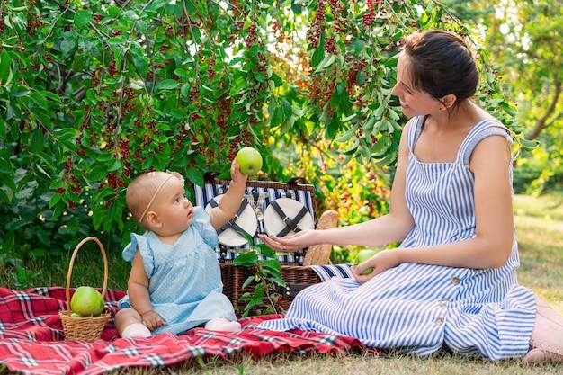 Bébé nouveau-né et maman dans une robe bleue lors d'un pique-nique. Un bambin de 9 à 12 mois tend une grosse pomme verte à sa mère