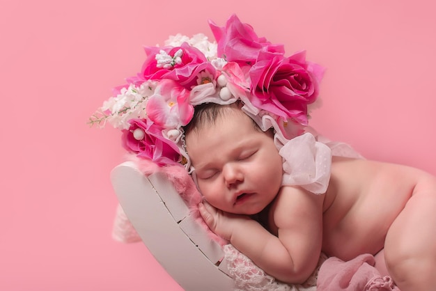 Le bébé nouveau-né mignon dort avec des fleurs sur un fond rose