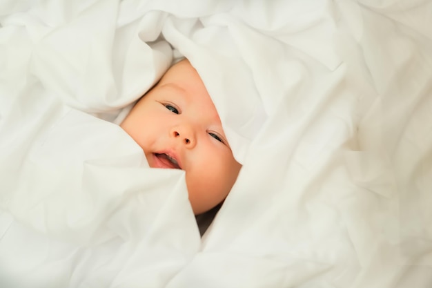 Le bébé nouveau-né sourit et rit montre des émotions bébé se trouve sur un tissu blanc