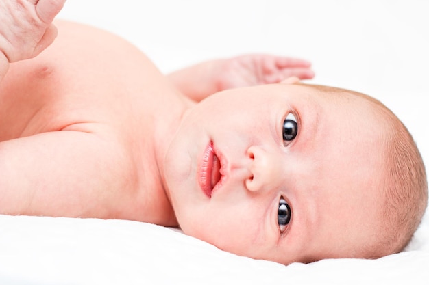 Le bébé nu est allongé sur le dos sur un drap blanc et montre des émotions Mise au point sélective sur la tête du bébé L'enfant regarde directement la caméra Gros plan