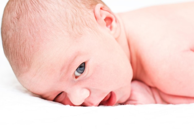 Le bébé nu est allongé sur le dos sur un drap blanc et montre des émotions Mise au point sélective sur la tête du bébé L'enfant regarde directement la caméra Gros plan