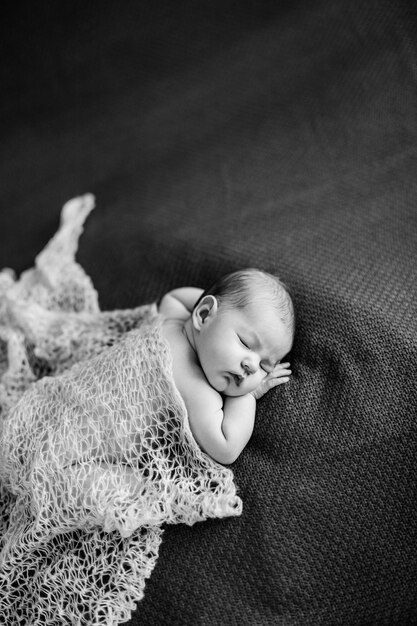 Bébé nu recouvert d'un châle dort sur une couverture photo noir et blanc