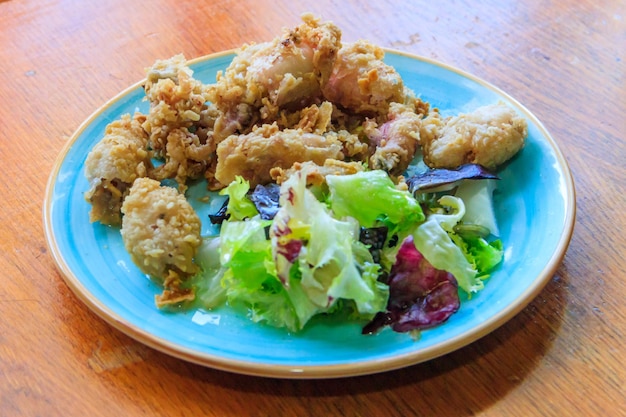 Un bébé pieuvre croustillant et frit servi avec de la salade sur une table en bois