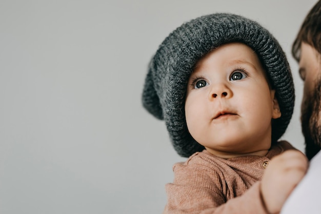 Bébé portant un bonnet tricoté surdimensionné gris sur fond de mur blanc