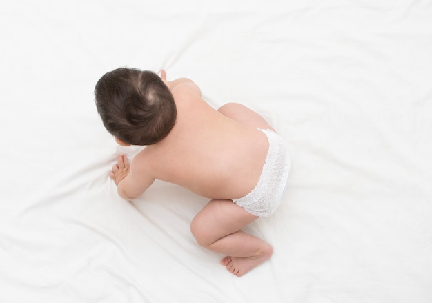 Bébé porte une couche jetable blanche rampant sur la couverture, vue de dessus