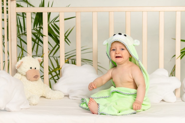 Bébé qui pleure dans une serviette verte après le bain sur le lit à la maison