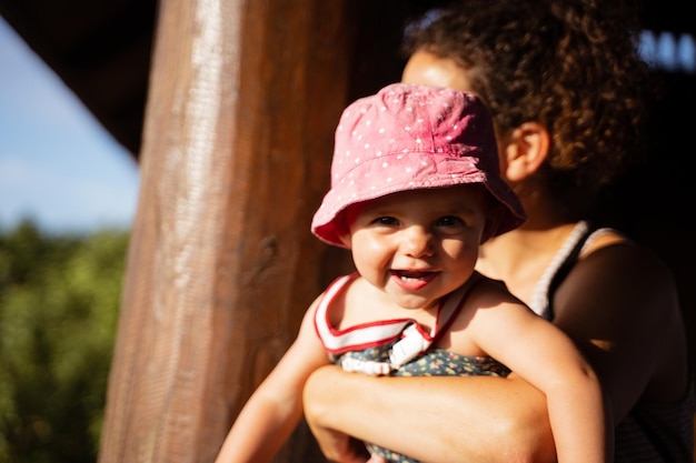 Bébé regarde la caméra pendant que sa mère l'embrasse à l'extérieur