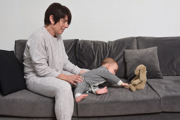 Bébé avec sa mère assise sur le canapé le bébé veut prendre la poupée