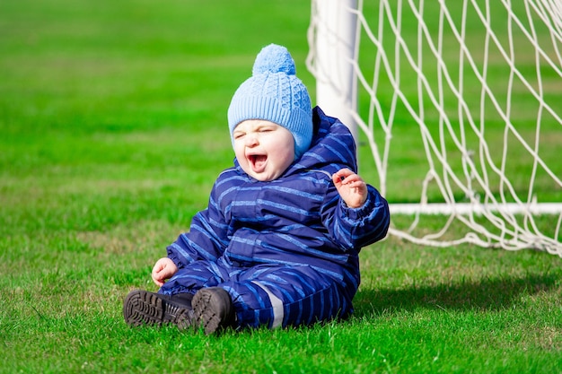 Bébé en salopette bleue est assis sur le terrain de football à l'objectif