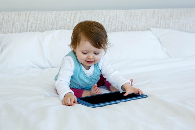 bébé souriant jouant avec une tablette sur un lit