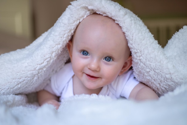 Bébé souriant regardant la caméra sous une serviette de couverture blanche