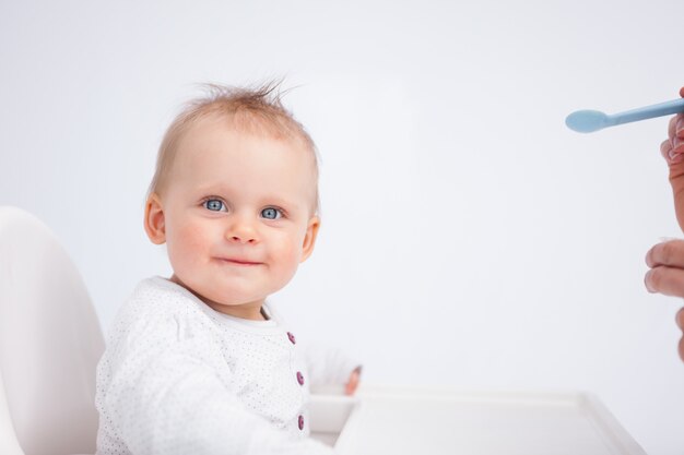 Bébé souriant en regardant la caméra tout en étant nourri sur un fond gris