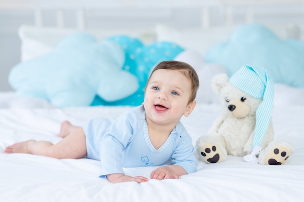 Bébé souriant ou riant sur le lit pour dormir avec un ours en peluche, intérieur de la chambre de bébé, petit bébé heureux en bonne santé