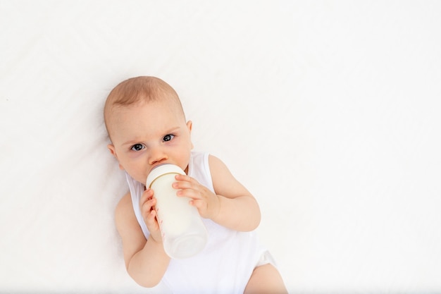 Bébé suce le lait d'une bouteille couchée dans un berceau dans la crèche sur un lit blanc