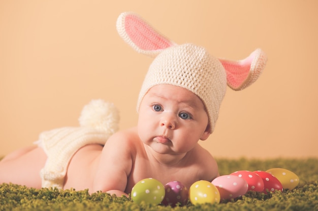 Bébé de trois mois allongé sur le ventre comme un lapin de Pâques sur l'herbe avec des œufs