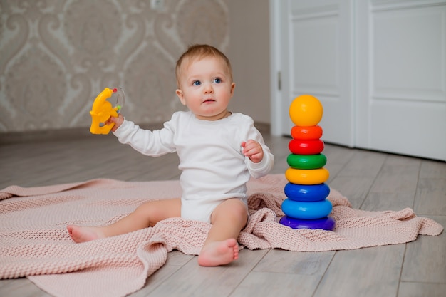 bébé en vêtements blancs assis sur le sol sur une couverture tricotée et jouant avec des jouets éducatifs, espace pour le texte