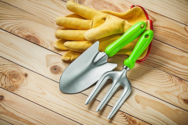 Bêche à main et fourche de jardin avec des gants en cuir jaune sur bois