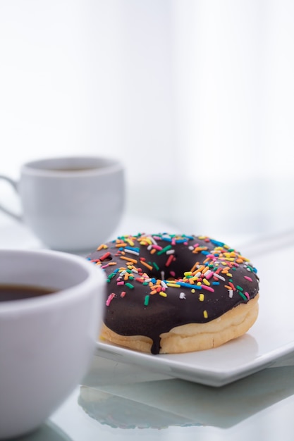 Beignet au chocolat arrose sur une plaque blanche et une tasse de café