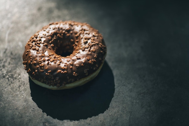 Beignet au chocolat glacé et saupoudré sur une table sombre