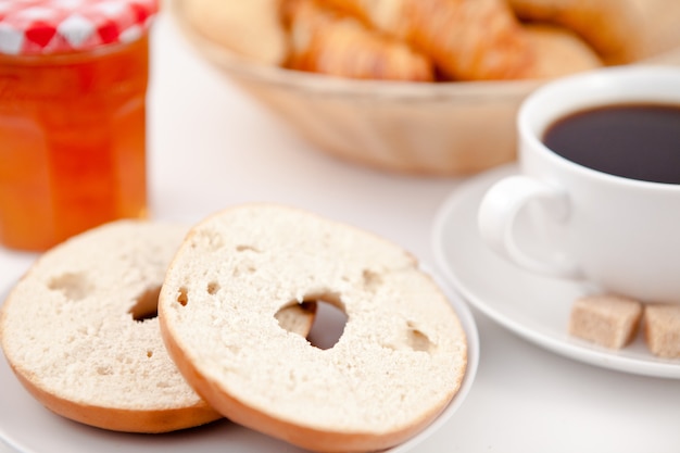 Beignet coupé en deux et une tasse de café sur des assiettes blanches avec du sucre et du lait et un pot de confiture