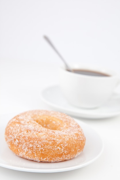 Photo beignet avec du sucre glace et une tasse de café avec une cuillère sur des plaques blanches