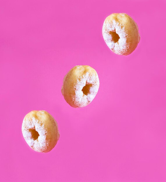 Beignet fait maison avec du sucre en poudre en mouvement tombant sur le fond rose Closeup Copy space