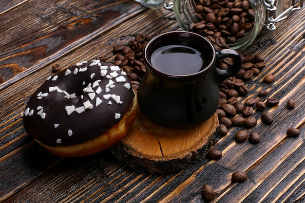 Beignet avec glaçage noir et chocolat en poudre et une authentique tasse de café fort. Une boîte de grains de café et de céréales coulées.