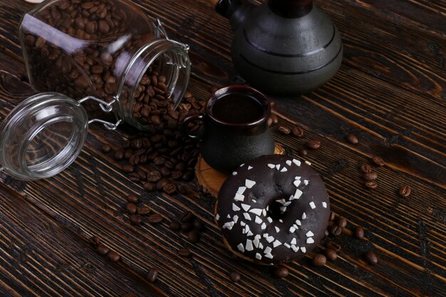 Beignet avec glaçage noir et chocolat en poudre et une authentique tasse de café fort. Une boîte de grains de café et de céréales coulées.