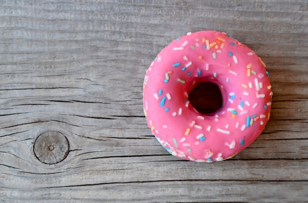 Beignet avec glaçage rose sur fond en bois avec un espace pour le texte. Mise à plat. Concept alimentaire Minimalisme Vue de dessus.