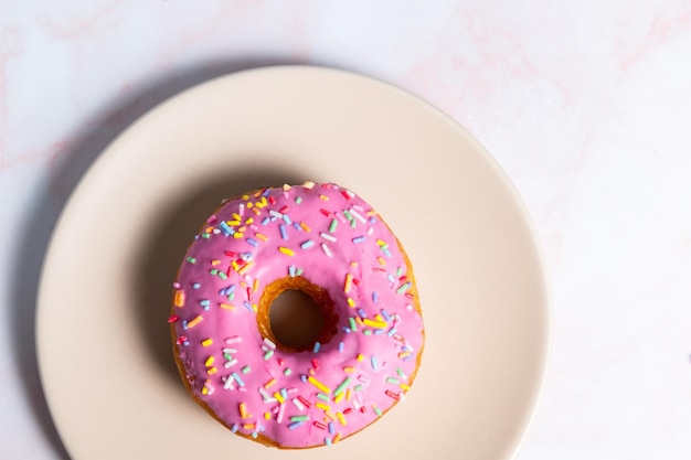 Beignet avec glaçage rose et pépites colorées sur la plaque Vue de dessus