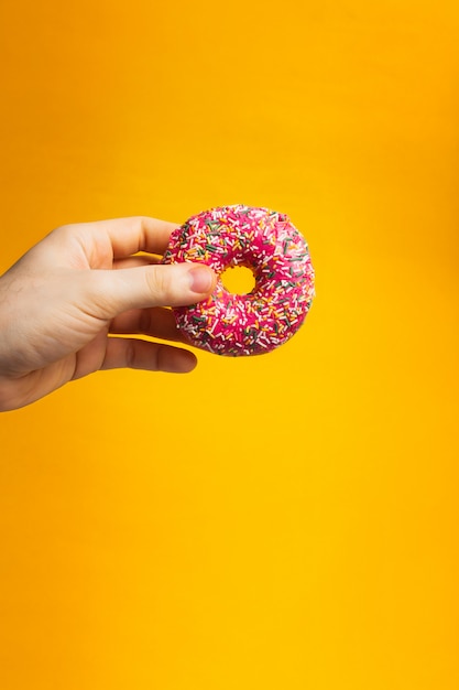 Beignet rose dans une main sur fond jaune