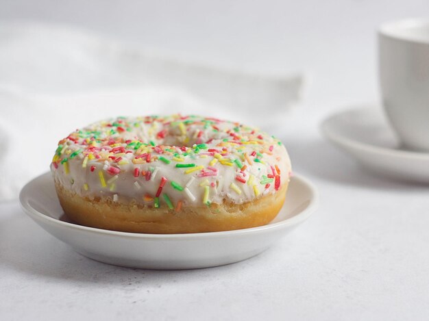 Le beignet à la vanille est dans une soucoupe sur la table. Il y a une serviette derrière. Il y a une tasse à proximité.